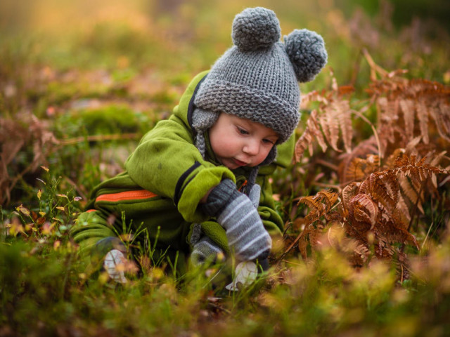 Małe dziecko w czapce i rękawiczkach bawi się jesienią w parku
