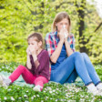 Mama i córka z alergią siedzą na trawie wśród stokrotek i dmuchają nos, Aleric spray do nosa na alergię