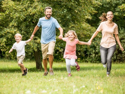 Szczęśliwa czteroosobowa rodzina biegnie wiosną parku, trzyma się za ręce