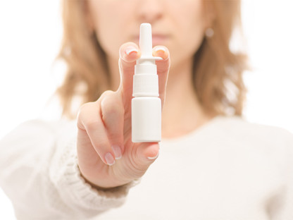 Kobieta pokazuje spray do nosa, w tle jej zamazana twarz, lek na alergię Aleric